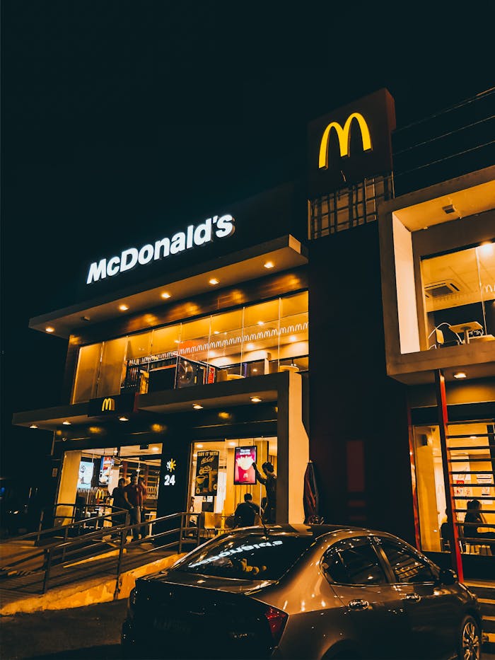 Exterior view of McDonald's in Cauayan City, Philippines illuminated at night with cars and people.